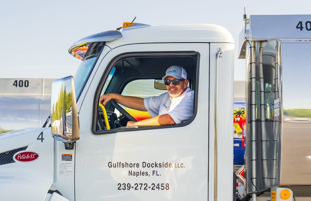 A Gulfshore Dockside driver at the wheel of a white Peterbilt tanker, the company name and phone on the cab door, Naples, Florida